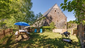 Un edificio in pietra con tetto spiovente, circondato da un prato con un tavolo da picnic e un barbecue.