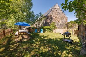 A stone building with a sloped roof, surrounded by a grassy yard with a picnic table and a barbecue grill. - Maison Paulette - Belle maison pour 8 en altitude (Neussargues en Pinatelle)