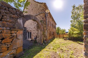 A stone building with an archway entrance, a wooden fence, and a lamp post. - Maison Paulette - Belle maison pour 8 en altitude (Neussargues en Pinatelle)