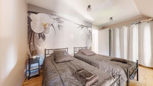 Camera da letto con due letti, un comodino, una parete con carta da parati floreale e una finestra con tende.