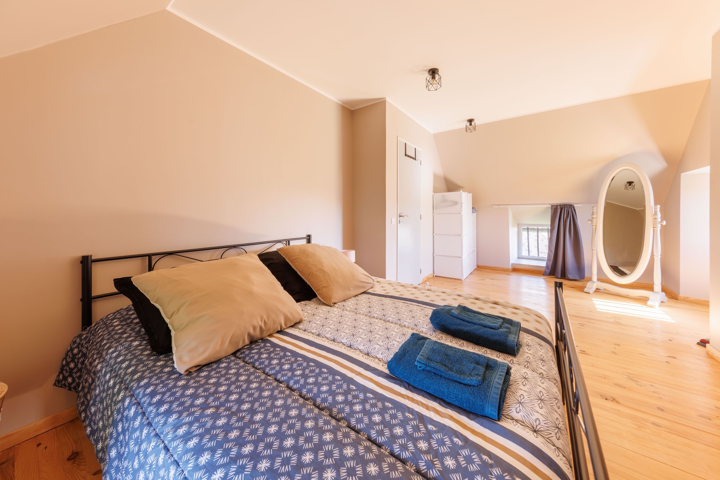 Een slaapkamer met een bed, kussens, een spiegel en een deur naar een andere kamer.