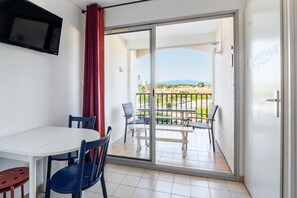 A balcony with a table and chairs, a TV mounted on the wall, and a view of a distant landscape. - Les Capitelles - Avec accès direct à la plage (Saint-Cyprien)