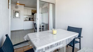 Un balcone con tavolo, sedie, una porta vetrata che dà su una cucina e una ventola a soffitto.