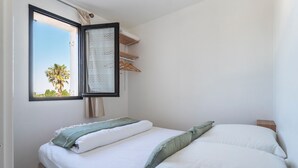 Una camera da letto con un letto, una finestra vista palme, un'asta appendiabiti e un comodino.