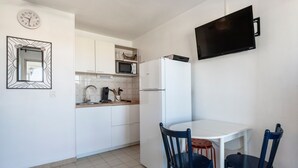 Una cucina compatta con mobili bianchi, un forno a microonde, un frigorifero, un tavolo da pranzo con due sedie e una TV a parete.