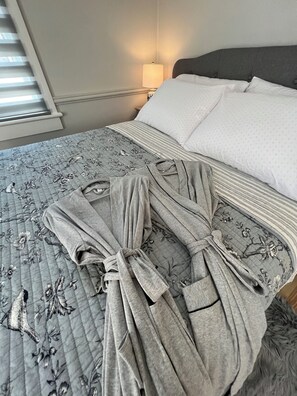 Un lit bien fait, avec une couette à motifs floraux, un peignoir gris posé sur le lit et une lampe de chevet.