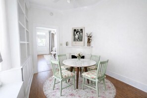 Een eetgedeelte met een ronde tafel, bloemenstoelen, een witte open haard en een ingelijst schilderij erboven.