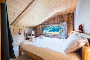 A wooden cabin bedroom with a bed, window, and wooden walls. - Cocon des Aravis - Beau duplex avec balcon (Le Grand Bornand)