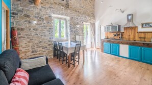 A rustic interior with a stone wall, wooden ceiling beams, a dining area, and a kitchen with blue cabinets. - Les Magnans - Grospierres (Grospierres)