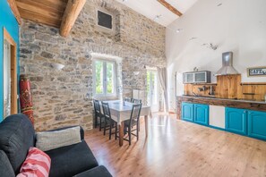 Ein rustikales Interieur mit Steinwand, Holzbalkendecke, Essbereich und Küche mit blauen Schränken.