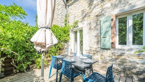 A stone building with a wooden deck, outdoor table with chairs, and a pergola with a canopy. - Les Magnans - Grospierres (Grospierres)