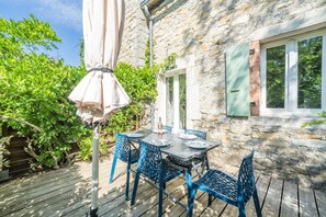 Ein Steinhaus mit einer Holzterrasse, einem Gartentisch mit Stühlen und einer Pergola mit Dach.
