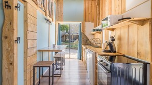 A kitchen with wooden walls, a dining area with a table and chairs, and a view of the outside. - Le Cocon - Grospierres (Grospierres)