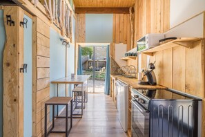 A kitchen with wooden walls, a dining area with a table and chairs, and a view of the outside. - Le Cocon - Grospierres (Grospierres)