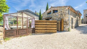 A stone building with a wooden gate, a glass structure with curtains, and a gravel driveway. - Le Cocon - Grospierres (Grospierres)