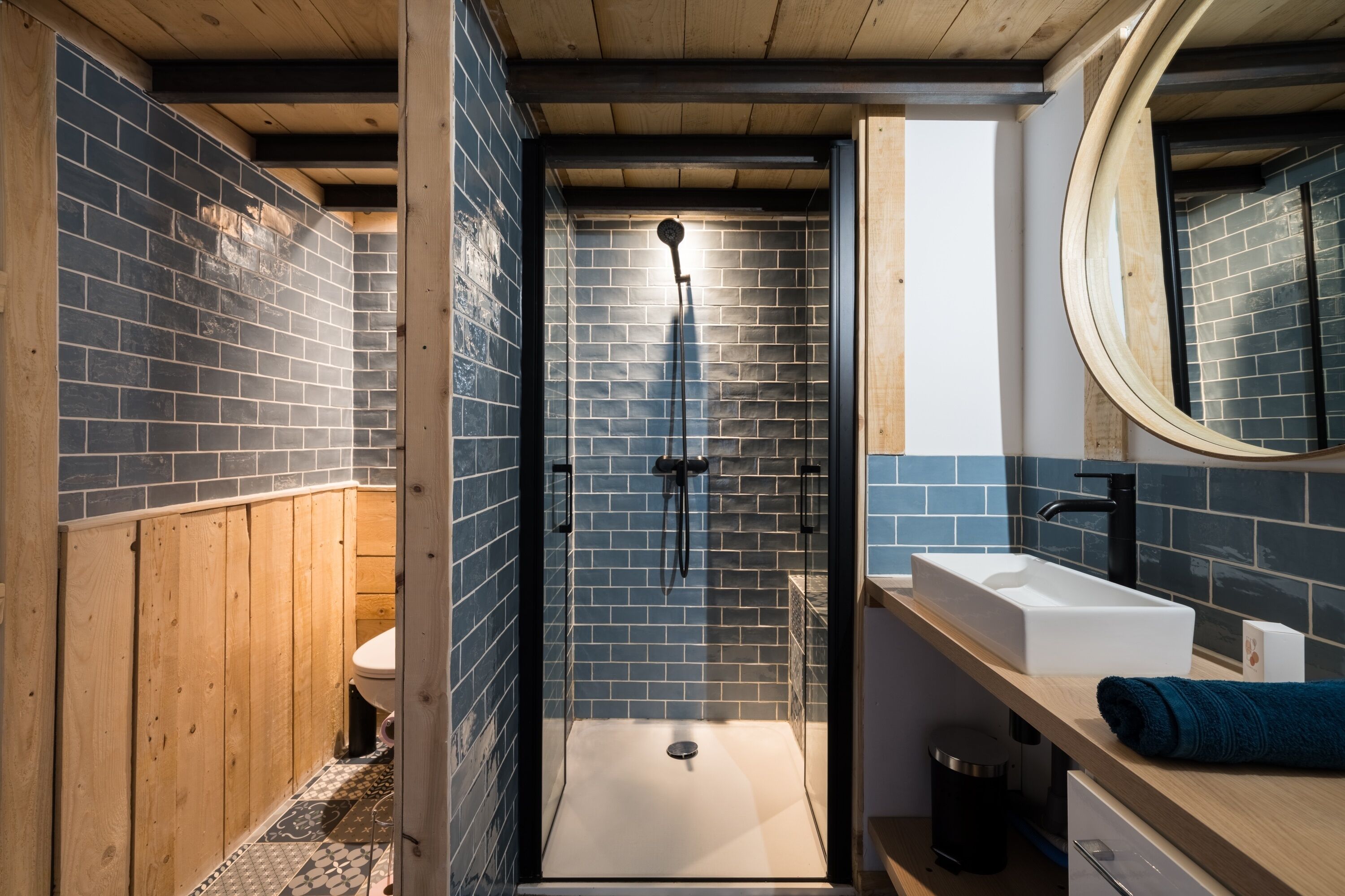 A modern bathroom with a glass-enclosed shower, a wooden vanity, and a large mirror.