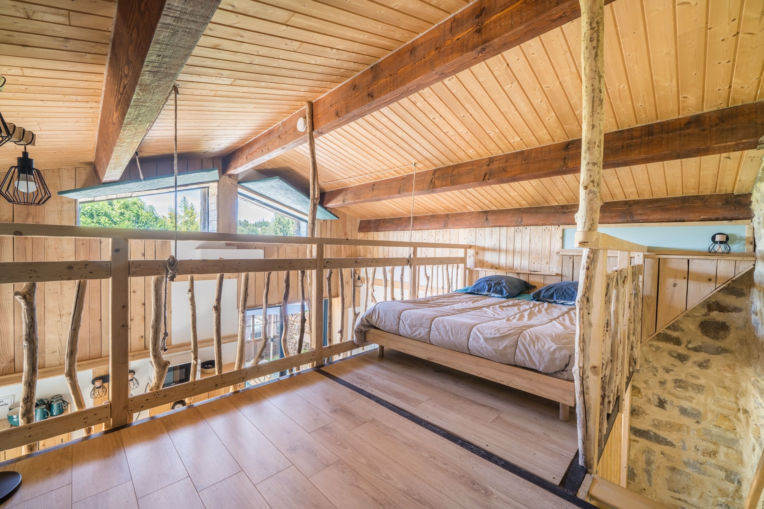 Interior de una cabaña de madera con cama, vigas de madera y un balcón.