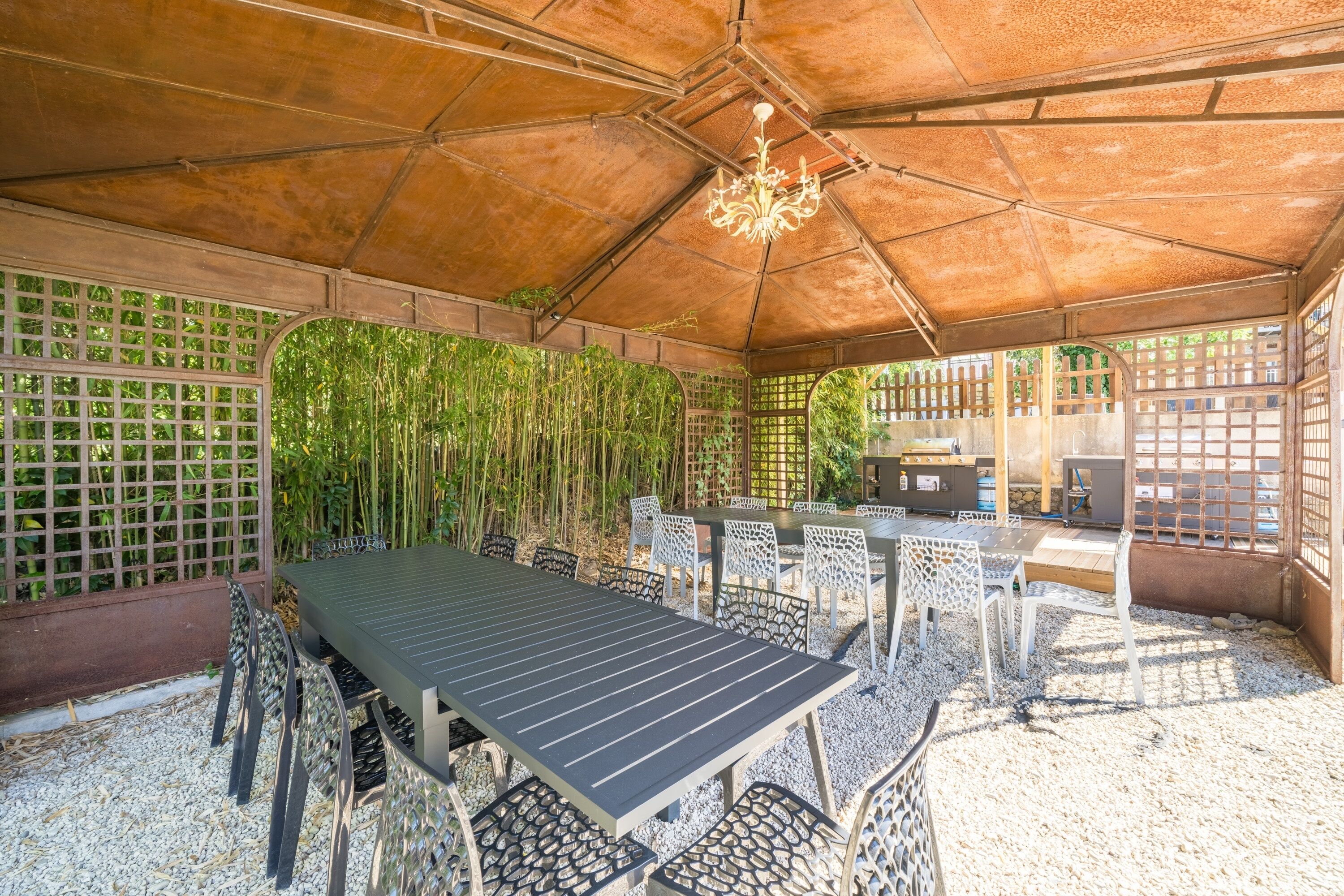 Un espace extérieur abrité, aménagé pour les repas, avec une table et des chaises, un barbecue et un décor en bambou.