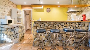 A kitchen with a stone wall, wooden countertop, and bar stools. - Le Studio - Grospierres (Grospierres)