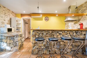 Une cuisine avec un mur en pierre, un plan de travail en bois et des tabourets de bar.