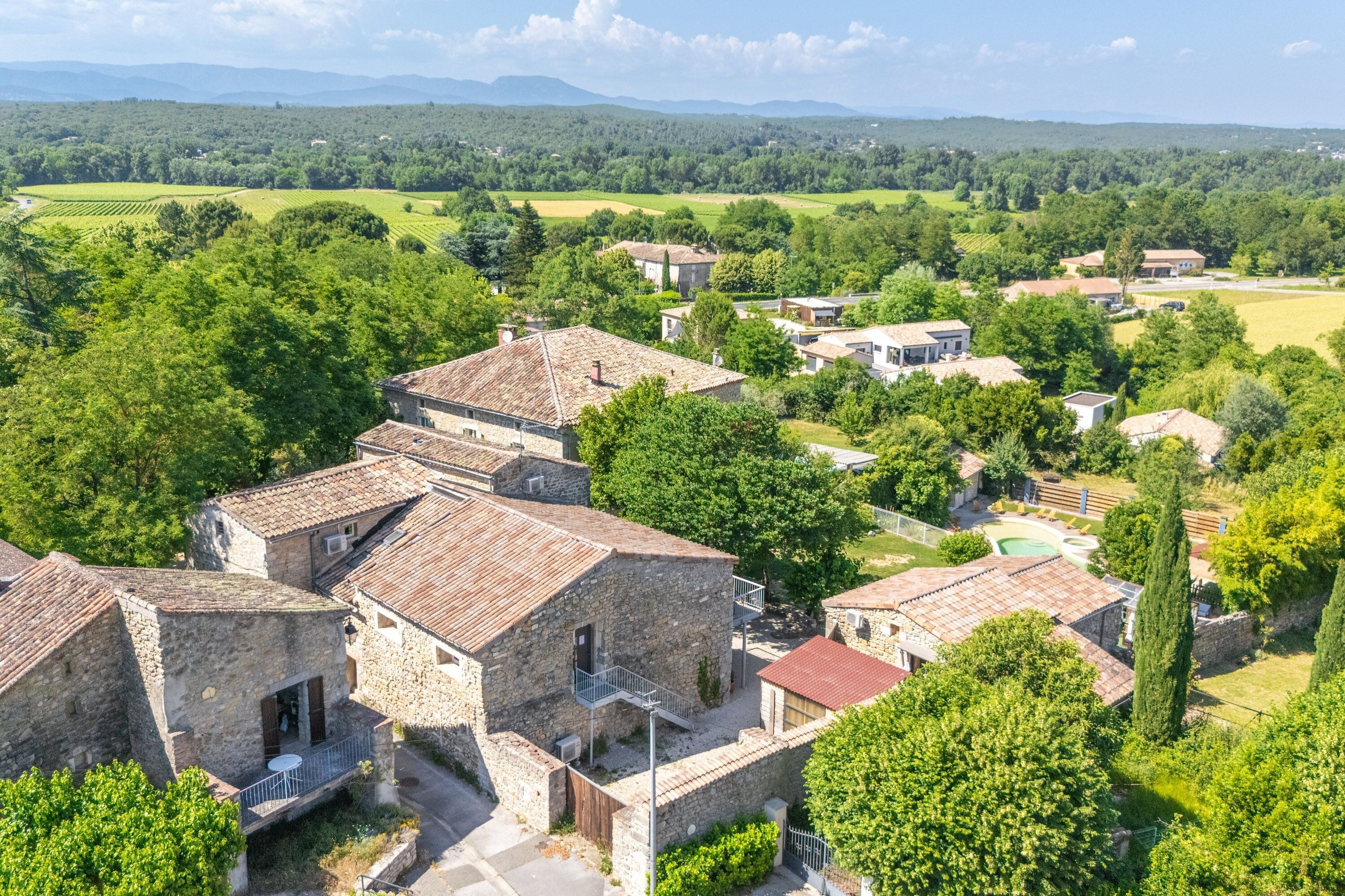 A rural village with stone buildings, a swimming pool, and surrounding greenery.