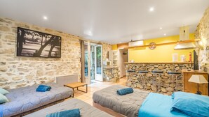 A room with two beds, a stone wall, a kitchen area, and a view through an open door. - Le Studio - Grospierres (Grospierres)