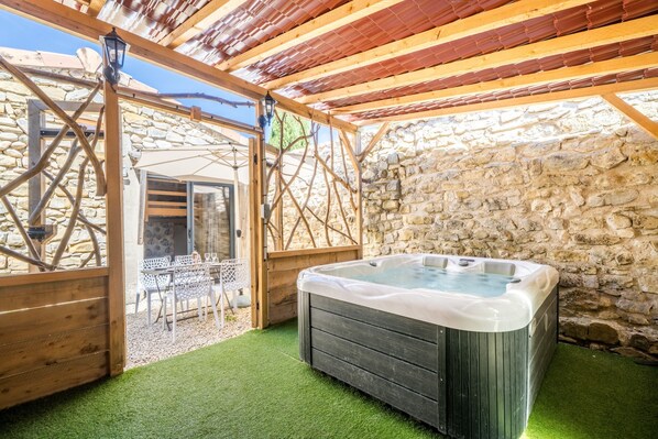 Ett bubbelbad i ett avskärmat utomhusområde med stenmurar och en träpergola.
