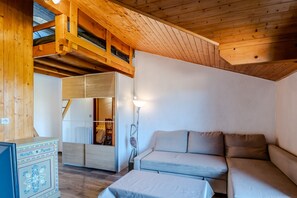 Ein gemütliches Zimmer mit Holzbalkendecke, einer Couch, einem Schrank und einer Lampe.