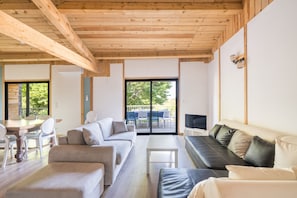 A modern living room with a wooden ceiling, a sofa set, a TV, and a dining area with chairs and a table. - Le Mûrier - Grospierres (Grospierres)