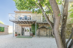 A stone building with a balcony, a door, and a potted plant. - Le Mûrier - Grospierres (Grospierres)