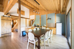 Een ruime keuken met houten balken, een eettafel met stoelen, en een trap naar een hoger gelegen verdieping.