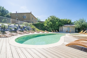 A wooden deck with a swimming pool, lounge chairs, and a stone building in the background. - Le Mûrier - Grospierres (Grospierres)