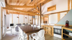 Ein geräumiger Essbereich mit Holztisch und weißen Stühlen, eine Küche mit Holzschränken und eine Erkerwohnung zum Schlafen.