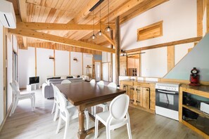 A spacious dining area with a wooden table and white chairs, a kitchen with wooden cabinets, and a lofted sleeping area. - Le Mûrier - Grospierres (Grospierres)