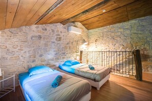 A bedroom with two beds, stone walls, wooden ceiling beams, and a small table. - La Magnanerie - Grospierres (Grospierres)