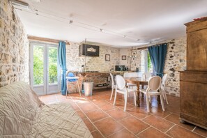 A cozy room with a bed, a dining table with chairs, a kitchen area, and a stone wall. - La Magnanerie - Grospierres (Grospierres)