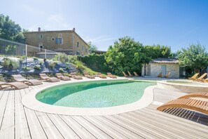 A wooden deck with a swimming pool, lounge chairs, and a stone building in the background. - La Magnanerie - Grospierres (Grospierres)