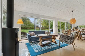 A spacious living room with a fireplace, a sofa, a dining table, and a chair. - Holiday home with large doors and forest (Gilleleje)