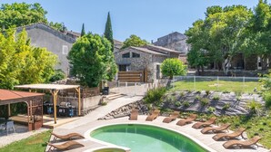 Piscina com espreguiçadeiras, uma pérgula e um edifício de pedra ao fundo.