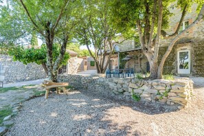 A stone building with a stone wall, a wooden bench, and a gravel area. - Le Mas - Grospierres (Grospierres)