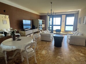 A living room with a TV, white sofas, a dining table, and a view through a large window. - Vrbo Property (Ajaccio)