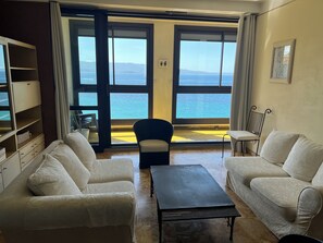 Ett vardagsrum med två soffor, ett soffbord och utsikt över havet genom stora fönster.