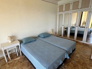 A bedroom with two beds, a nightstand, a lamp, and a wardrobe with a mirror. - Vrbo Property (Ajaccio)