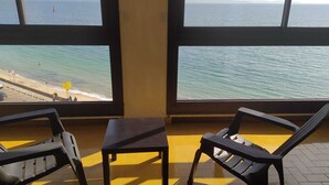 Ein Zimmer mit großen Fenstern und Meerblick, zwei Plastikstühle und ein kleiner Tisch.