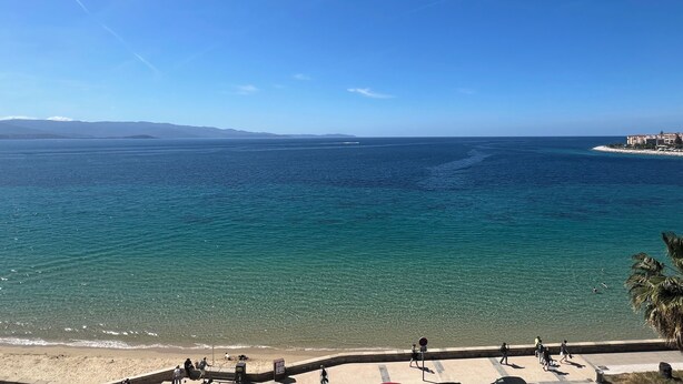 Blick auf die Küste mit blauem Himmel, Sandstrand und ruhiger See.