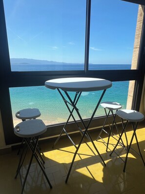 A room with a large window, a round table, and four stools. - Vrbo Property (Ajaccio)