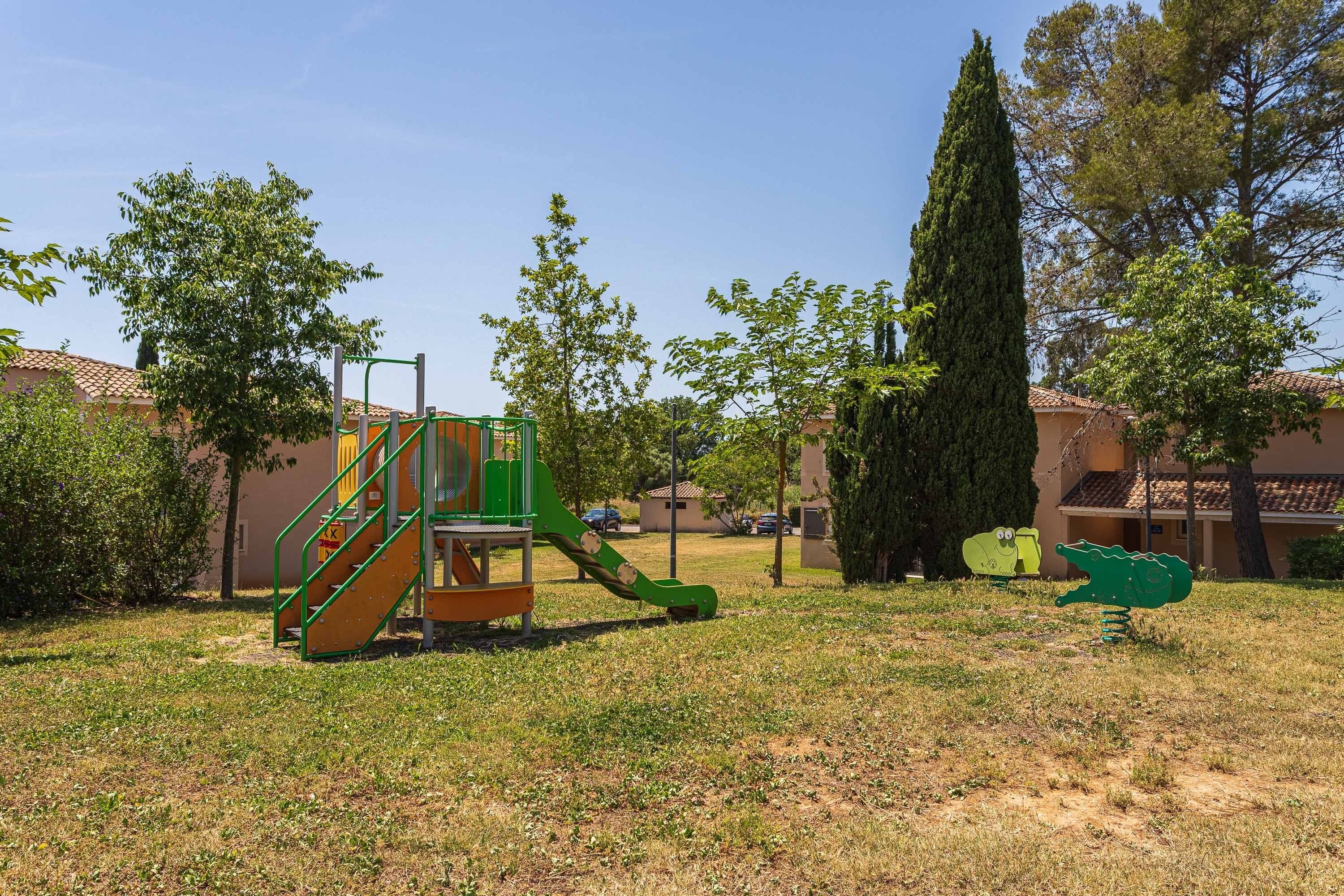 A playground with a slide and climbing structure, surrounded by trees and buildings.