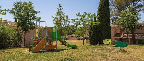 A playground with a slide and climbing structure, surrounded by trees and buildings.