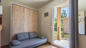 Ein Zimmer mit grauem Sofa, einer Wand aus Holzpaneelen und einer Glasschiebetür, die zu einem Außenbereich führt.