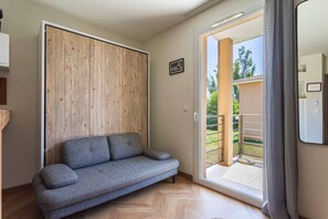 Ein Zimmer mit grauem Sofa, einer Wand aus Holzpaneelen und einer Glasschiebetür, die zu einem Außenbereich führt.